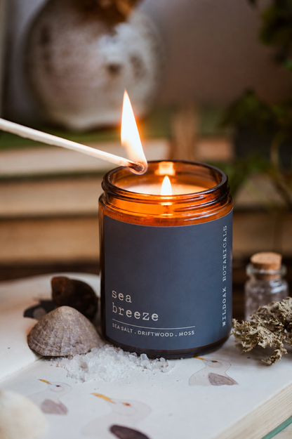Sea Breeze soy candle by WILDOAK BOTANICALS. with sea salt and driftwood scent, featuring a white candle in an amber glass jar.