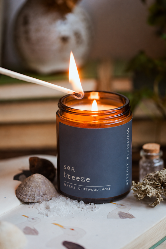 Sea Breeze soy candle by WILDOAK BOTANICALS. with sea salt and driftwood scent, featuring a white candle in an amber glass jar.